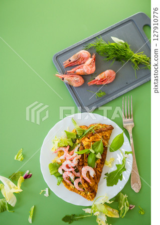 Fried omelette with shrimps and greens on a green background 127910776