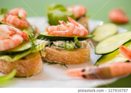 Appetizing appetizers with shrimps, sauce and cucumbers on a green background Appetizing appetizers with shrimps, sauce and cucumbers on a green background 127910787