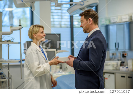 Pharmaceutical sales representative handing a sample box of new medication to female doctor. 127911027