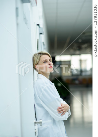 Tired female doctor leaning against wall in hospital hallway. Tired female doctor leaning against wall in hospital hallway. 127911036