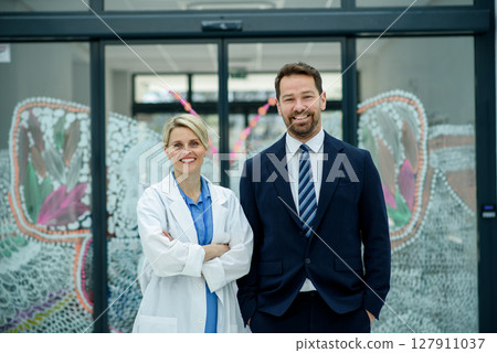 Male hospital manager standing next to female doctor, medical setting. 127911037