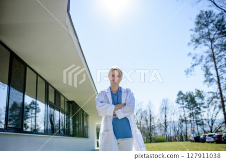 Young female doctor taking a break, standing in front of hospital. Young female doctor taking a break, standing in front of hospital. 127911038