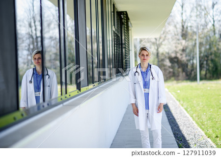 Young female doctor taking a break, standing in front of hospital. Young female doctor taking a break, standing in front of hospital. 127911039