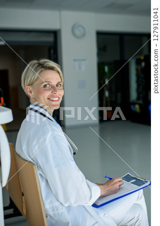 Young female doctor with short hair in sitting on bench in hospital corridor. Young female doctor with short hair in sitting on bench in hospital corridor. 127911041