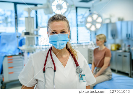 Doctor in face mask standing in examination room. 127911043
