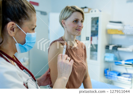 Doctor administering vaccine to woman's arm during routine immunization 127911044