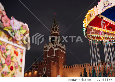 Spasskaya Tower of Moscow Kremlin shining at night with christmas market attractions surrounding it 127911136