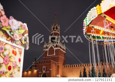 Spasskaya Tower of Moscow Kremlin shining at night next to carousel during christmas holidays 127911151