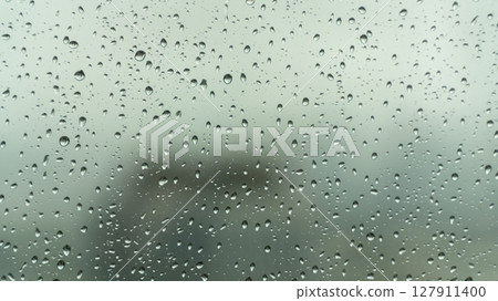 Close-up view of raindrops on a glass window during a rainy day, with a soft, blurry background creating a calm and moody atmosphere. 127911400