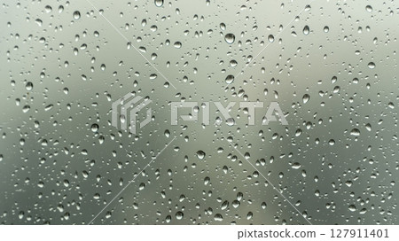 Close-up view of raindrops on a glass window during a rainy day, with a soft, blurry background creating a calm and moody atmosphere. 127911401