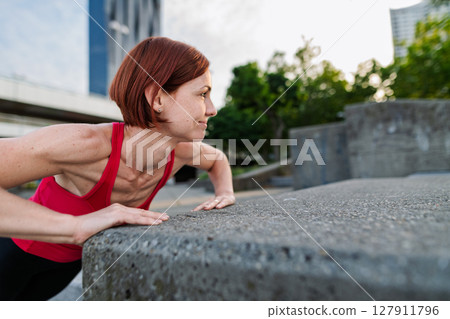 Woman working out in the city, doing bodyweight strength exercises outdoors 127911796