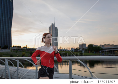 sporty woman running across a city bridge during her morning workout. 127911807