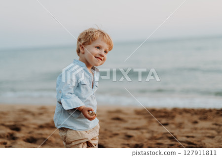 A small toddler boy standing on beach on summer holiday, having fun. 127911811