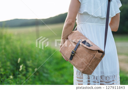 Woman fastening leather strap on stylish brown shoulder bag Woman fastening leather strap on stylish brown shoulder bag 127911843