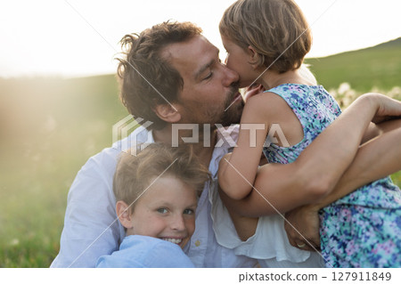 Young family with small children in summer nature at sunset, sitting in the grass. 127911849
