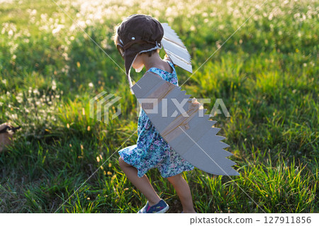 Little girl playing on a meadow in nature, with goggles and wings as if flying. Little girl playing on a meadow in nature, with goggles and wings as if flying. 127911856