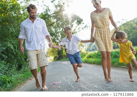 A young family with small children playing hopscotch on a road in summer. 127911866