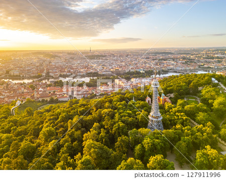 Golden light bathes the Petrin Lookout Tower in Prague. Surrounding greenery contrasts with the historic city skyline, capturing a tranquil morning at dawn over the vibrant park. Golden light bathes the Petrin Lookout Tower in Prague. Surrounding greenery contrasts with the historic city skyline, capturing a tranquil morning at dawn over the vibrant park. 127911996