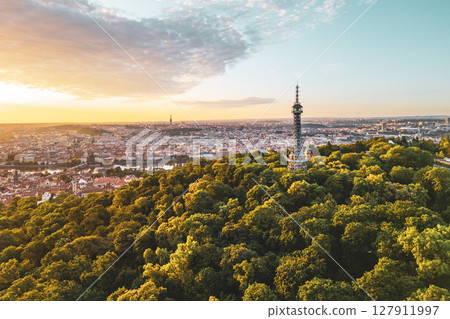 Petrin Lookout Tower rises majestically over Prague at sunrise, surrounded by lush greenery. The cityscape glows warmly as the first light of day illuminates the historic skyline. Petrin Lookout Tower rises majestically over Prague at sunrise, surrounded by lush greenery. The cityscape glows warmly as the first light of day illuminates the historic skyline. 127911997