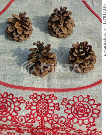 Four pine cones on a decorative burlap with embroidery 127912330