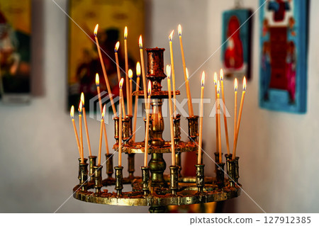 Lit prayer candles burn on traditional stand inside old church surrounded by religious icons. Concept of spirituality, prayer, quiet connection through sacred ritual and inner peace Lit prayer candles burn on traditional stand inside old church surrounded by religious icons. Concept of spirituality, prayer, quiet connection through sacred ritual and inner peace 127912385