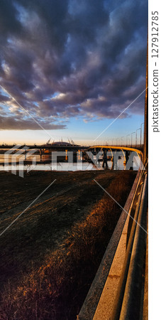 Scenic view of a bridge bathed in golden sunset light, highlighting the pathway designed for cyclists. The tranquil setting reflects a peaceful evening mood with clear skies 127912785
