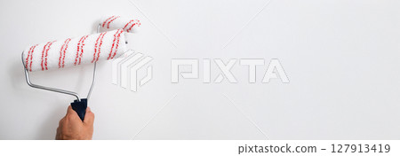 Banner of man using a small and large roller brush to paint wall edges, precise work during apartment makeover. 127913419