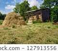 Countryside scenery with haystack among green grass meadow near old wooden hayloft barn at sunny summer day. With no people rural landscape, agricultural and country life theme. 127913556