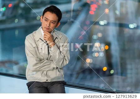 A man in work clothes thinking with his arms folded against a skyscraper in the background 127913629