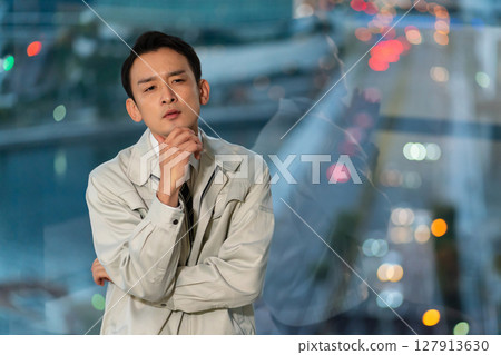 一位身著工作服的男子雙臂交叉，背對著摩天大樓思考著 127913630