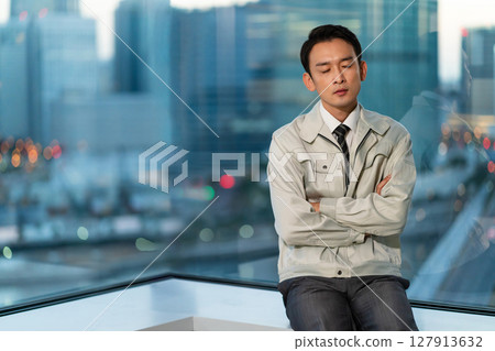 一位身著工作服的男子雙臂交叉，背對著摩天大樓思考著 127913632