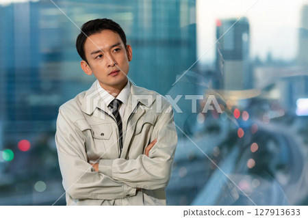 一位身著工作服的男子雙臂交叉，背對著摩天大樓思考著 127913633