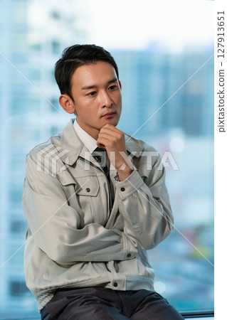 一位身穿工作服的男子一邊看著摩天大樓一邊思考 127913651