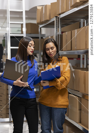 Asian staff members checking parcels at a startup fulfillment center. Local delivery and in house logistics supported by organized storage, taped boxes and efficient inventory management. Asian staff members checking parcels at a startup fulfillment center. Local delivery and in house logistics supported by organized storage, taped boxes and efficient inventory management. 127913884