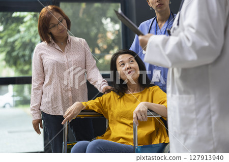 Healthcare medic supporting woman in wheelchair during routine appointment at inclusive clinic. Expert offering advice on maintaining wellness and adapting lifestyle around physical disability. 127913940