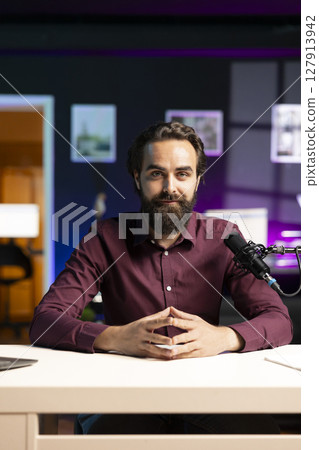 Portrait of influencer in home studio using professional microphone to record live broadcast for online streaming platforms, talking with fans. Smiling media star hosts q and a session with viewers Portrait of influencer in home studio using professional microphone to record live broadcast for online streaming platforms, talking with fans. Smiling media star hosts q and a session with viewers 127913942