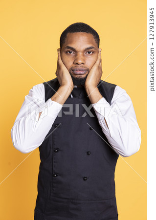African american waiter recreates the three wise monkeys proverb, showing the symbolic metaphor by covering his ears in studio. Young restaurant employee does wisdom symbol. African american waiter recreates the three wise monkeys proverb, showing the symbolic metaphor by covering his ears in studio. Young restaurant employee does wisdom symbol. 127913945