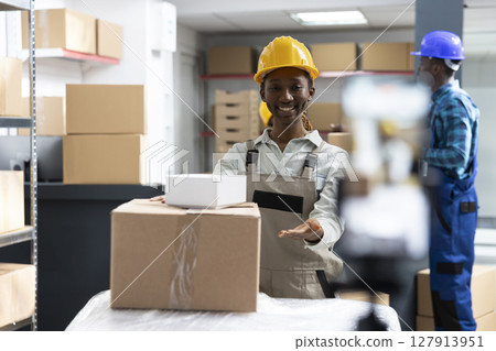 Employee recording a live tutorial in an industrial warehouse, showcasing product handling, packaging and shipment control. Creates video content for marketing and client reach. Employee recording a live tutorial in an industrial warehouse, showcasing product handling, packaging and shipment control. Creates video content for marketing and client reach. 127913951
