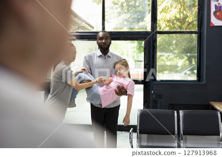 Panic sets in as father is carrying his unconscious little child in lobby, leading to quick intervention from doctor and nurse during emergency. Urgent medical needs and consultation. 127913968
