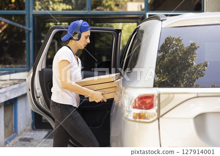 Female city courier carrying massive stack of pizza boxes delivering fast food order from a restaurant. Driving the courier service car to bring bigger meal orders, pizza delivery. Female city courier carrying massive stack of pizza boxes delivering fast food order from a restaurant. Driving the courier service car to bring bigger meal orders, pizza delivery. 127914001