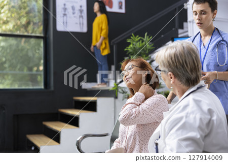 Doctor consulting patient about neck pain symptoms during medical appointment at hospital lobby. Healthcare staff discussing treatment plan and posture adjustments to relieve muscle strain. 127914009
