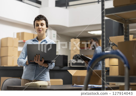 Woman employee working in a warehouse on order processing in small business depot, preparing taped boxes for local brand express delivery logistics. Distribution center supply room. Woman employee working in a warehouse on order processing in small business depot, preparing taped boxes for local brand express delivery logistics. Distribution center supply room. 127914043