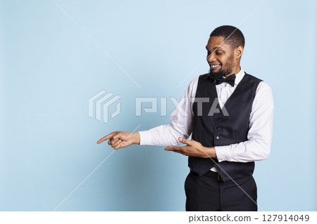 Doorkeeper bellhop pointing at something to left or right sides, indicating the direction for multiple amenities at the five star resort. Bellboy staff wearing a tuxedo uniform at his job. Doorkeeper bellhop pointing at something to left or right sides, indicating the direction for multiple amenities at the five star resort. Bellboy staff wearing a tuxedo uniform at his job. 127914049