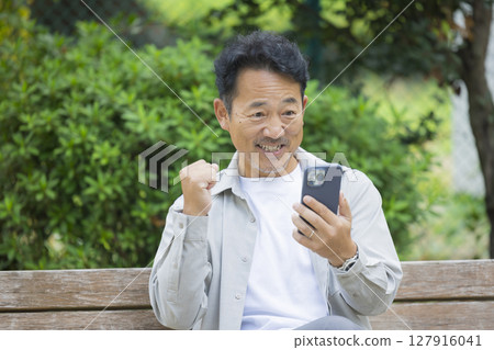 Senior man looking at his smartphone on a park bench Senior man looking at his smartphone on a park bench 127916041