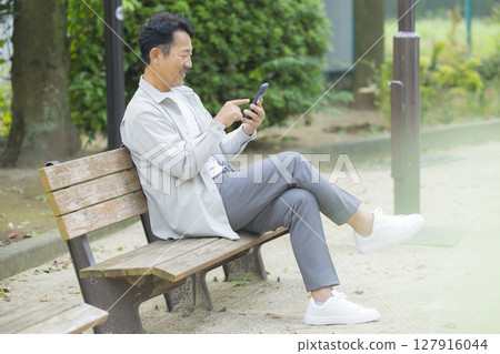 Senior man looking at his smartphone on a park bench Senior man looking at his smartphone on a park bench 127916044