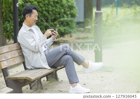 Senior man looking at his smartphone on a park bench 127916045