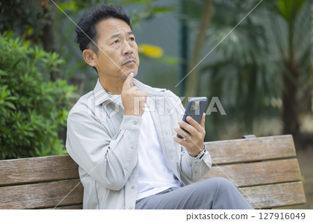 Senior man looking at his smartphone on a park bench 127916049