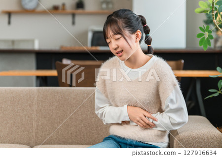一名小學或國中女孩因胃痛坐在家裡的沙發上摀著肚子 127916634