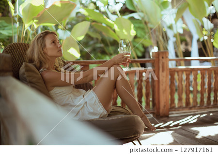 Young woman sit on open-air veranda of wooden bungalow with tropical garden view. Girl relaxing in luxury villa on family summer vacation. Tropical lifestyle. Young woman sit on open-air veranda of wooden bungalow with tropical garden view. Girl relaxing in luxury villa on family summer vacation. Tropical lifestyle. 127917161