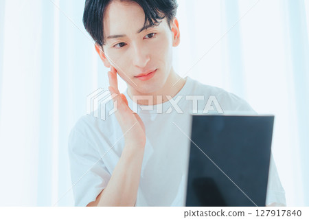 A refreshing guy checking his skin in the mirror — Men's skin care habits A refreshing guy checking his skin in the mirror — Men's skin care habits 127917840